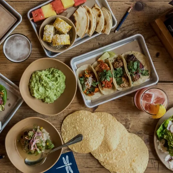 Overhead view of bartaco dishes including tacos, guacamole, grilled corn, and fresh beverages