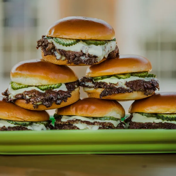 Stack of cheeseburgers with pickles and melted cheese on a green serving platter