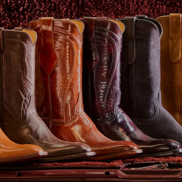 Row of handcrafted leather cowboy boots in assorted rich colors displayed on wooden shelf