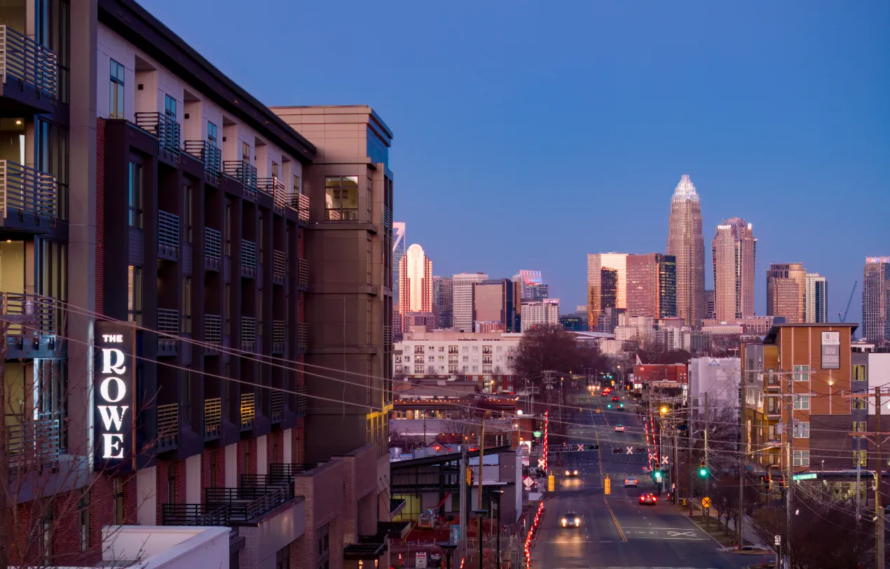 Urban street scene in Charlotte featuring The Rowe apartments and high-rise skyline backdrop