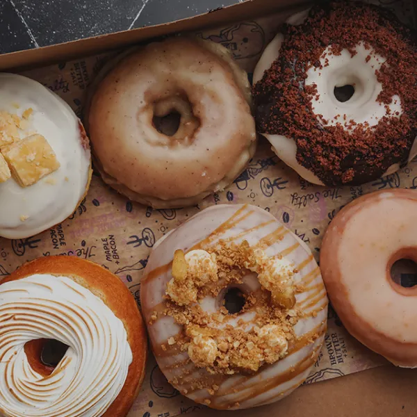 Assorted gourmet donuts with unique toppings including caramel drizzle, crumble, and frosting swirls