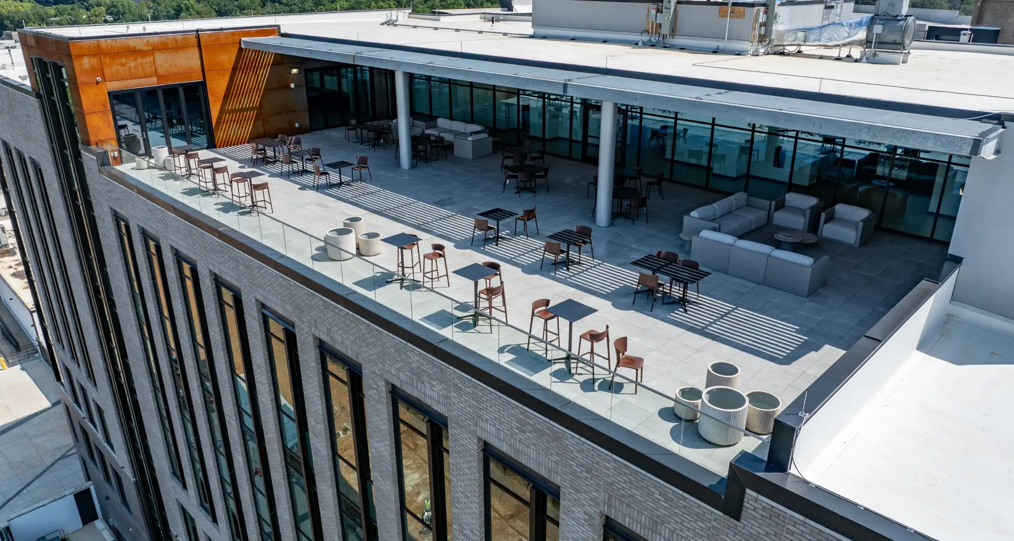 Aerial view of rooftop terrace with glass railing, lounge seating, and open-air dining tables