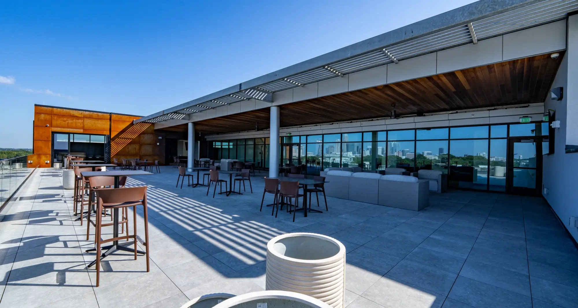 Rooftop lounge with shaded seating area and skyline reflections on glass wall enclosure